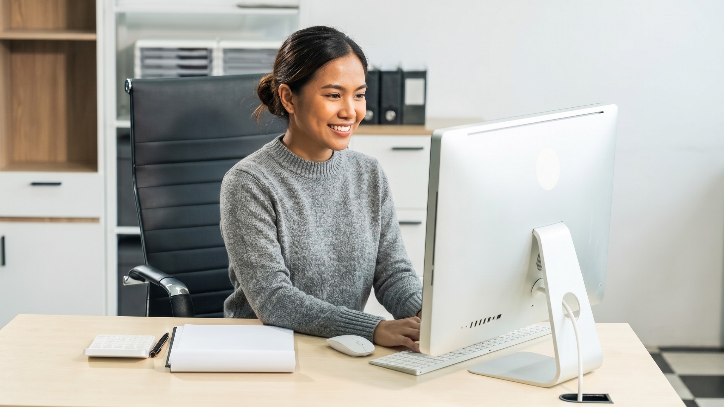 Filipina virtual production coordinator working on a desktop computer in an office setting