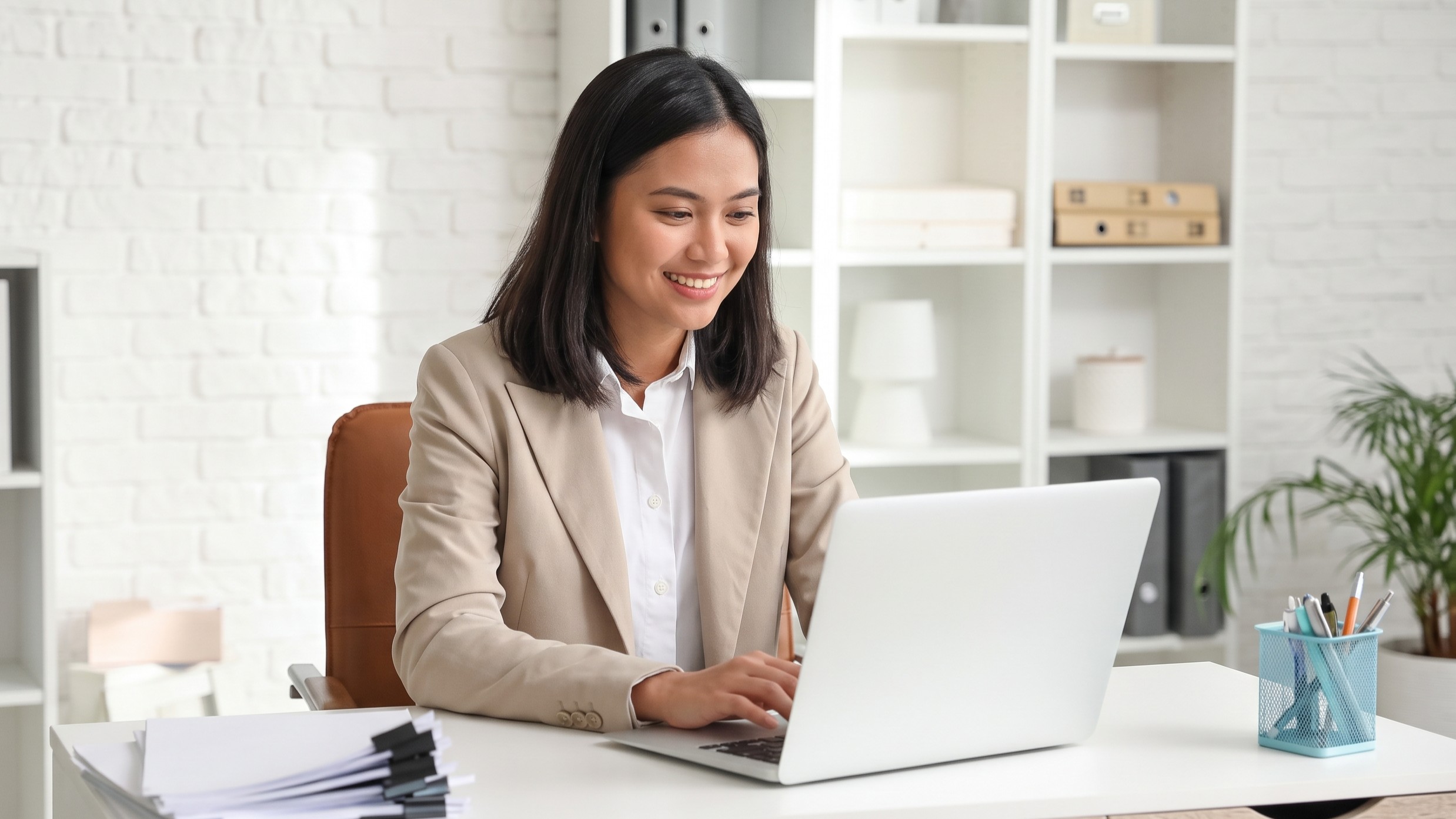 filipina remote claims officer working in a bright office with a laptop and documents on the desk