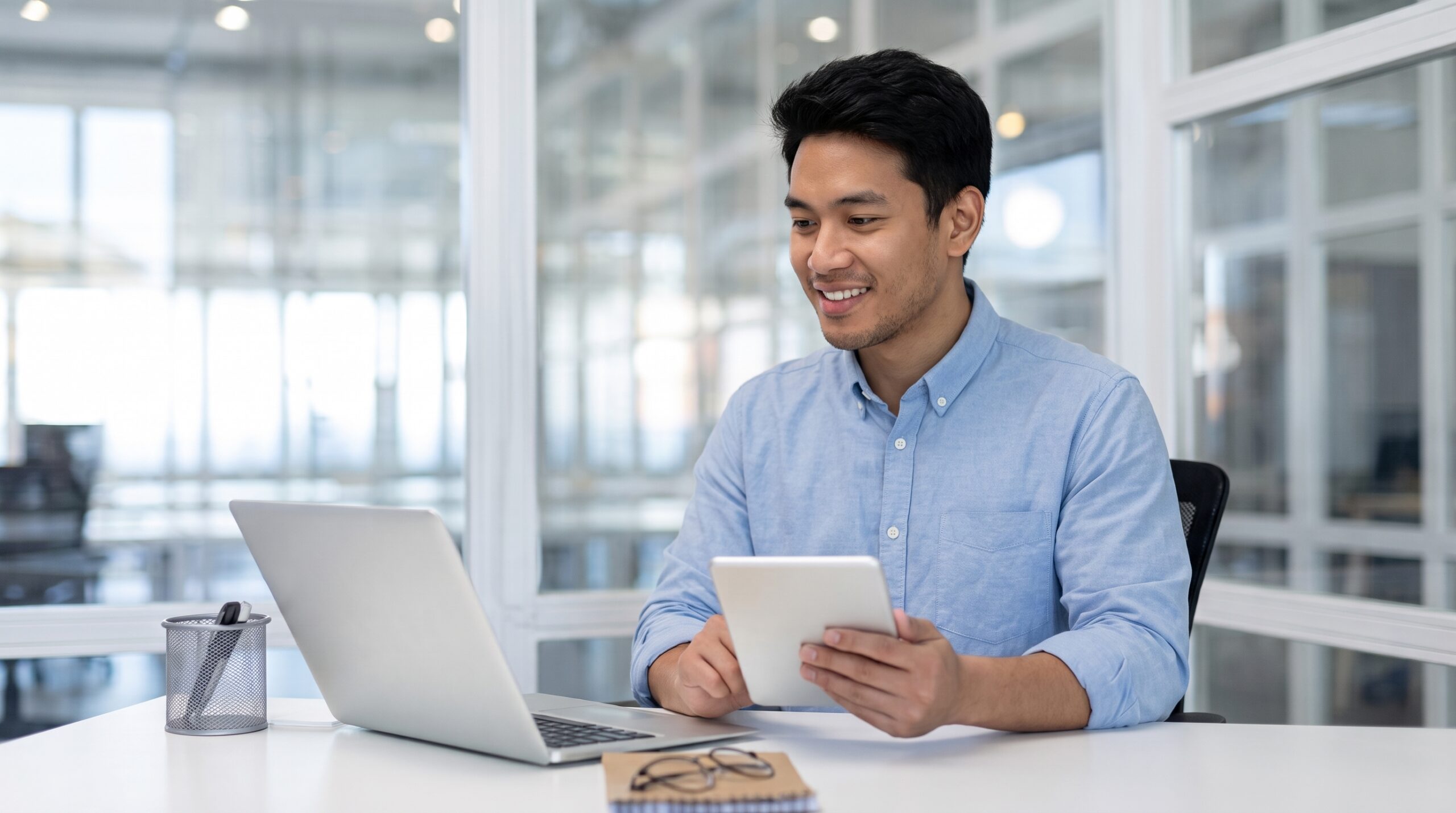 filipino sales engineer working in an office with a laptop and holding a tablet